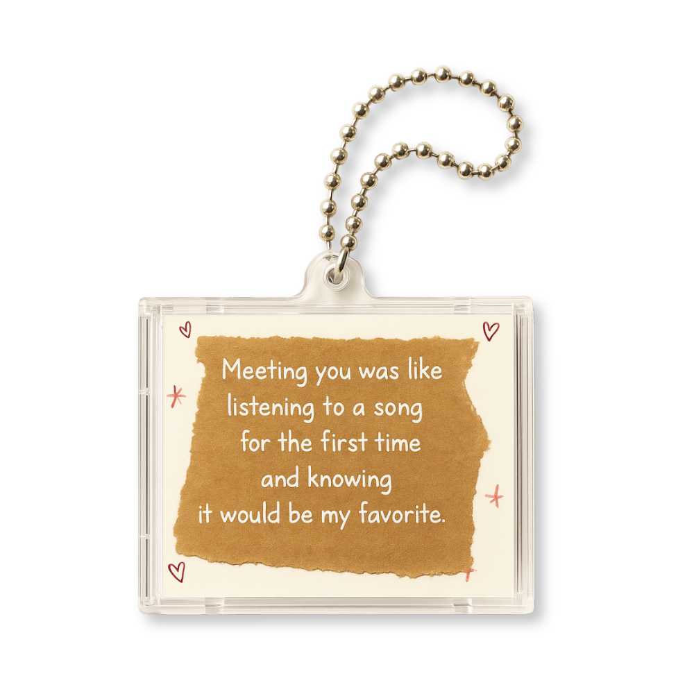 A transparent keychain features a brown paper-like background with the text, Meeting you was like listening to a song for the first time and knowing it would be my favorite, surrounded by small red hearts.